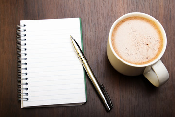 Blank notebook, pen and cup of coffee on wooden brown background, copy space.