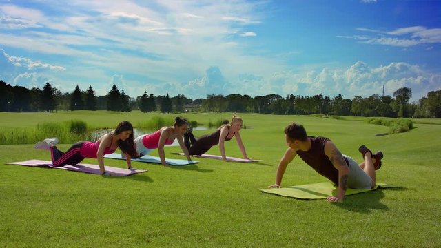 Happy friends outdoor training. Teenage people doing push ups at boot camp. Outdoor fitness group. Healthy lifestyle concept. Multi ethnic women doing push up exercise on green grass