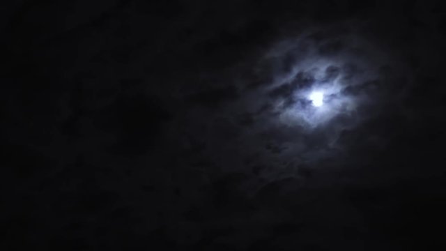 Moon hiding behind clouds in a black night sky