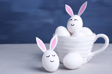 Easter eggs with paper ears on table against blue background