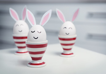 Easter eggs with paper ears on table against blurred background