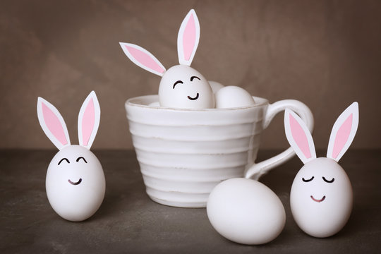 Easter eggs with paper ears and faces on table