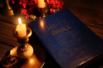 Bible and candle on wooden table, closeup