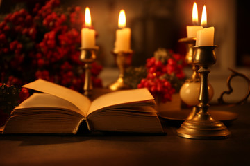 Open Bible and burning candles on table