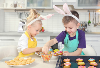 Cute little children decorating Easter cookies at kitchen