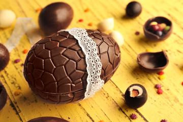 Chocolate Easter egg in cute lace ribbon and sweets on wooden background