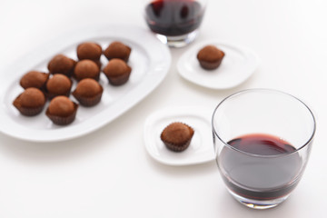 Delicious chocolate truffles and red wine on white background
