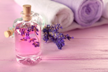 Obraz na płótnie Canvas Bottle with lavender aroma oil and towels on pink wooden background