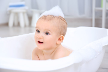 Little baby boy washing in bathtub indoors