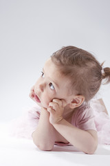 Portrait of Sad Looking Little Caucasian Blond Child Posing in Pink Dress Against White Background.