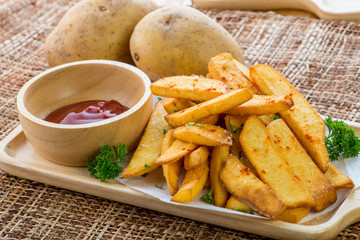 Tasty french fries on cutting board with ketchup, on wooden table background