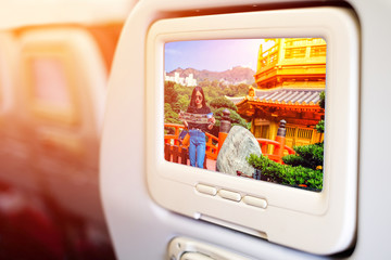 Aircraft monitor in front of passenger seat showing a woman reading a map of  Chi Lin Nunnery and Nan Lian Garden in Hong Kong