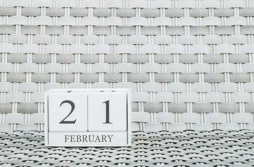 Closeup surface white wooden calendar with black 21 february word on blurred weave wood chair textured background with copy space in selective focus at the calendar