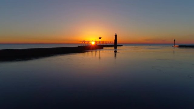 Scenic aerial flyby of Lake Michigan lighthouse, harbor at sunrise.
