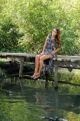 Attractive young woman sits on a wooden bridge outdoors
