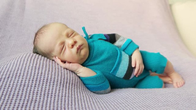 Lovely kid dressed in knitted blue costume, sleeping on his side, hand under hes cheek