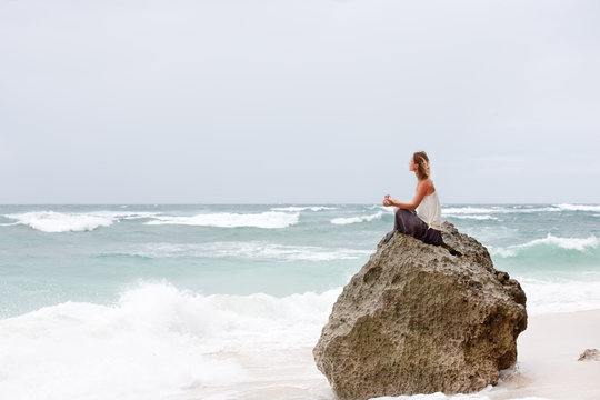 Girl sit at the seaside on the rock and meditating in yoga pose