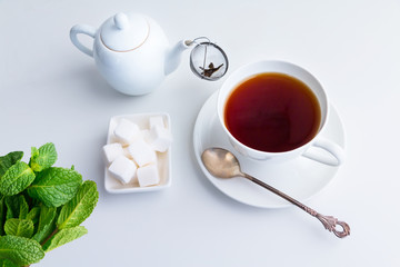 Cup of black tea, teapot with strainer and white sugar cubes.