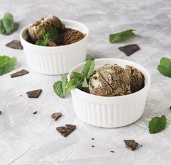 chocolateand  mint ice cream in white bowls with pieces of chocolate and mint leaves on a marble table