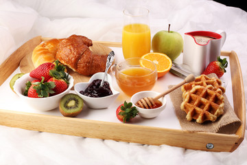 breakfast in bed with fruits and pastries on a tray -waffles, croissants, coffe and juice