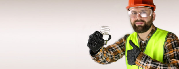 Worker in a helmet and protective clothing with a light bulb in a hand