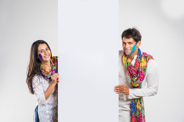 indian couple busy on smartphone on Holi festival, with face painted with colours or presenting...