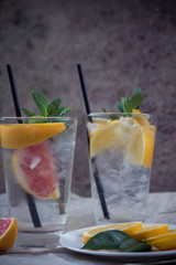 Two glass cups of water with red orange, lemon, mint and ice. Fresh lemonade