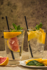 Two glass cups of water with red orange, lemon, mint and ice. Fresh lemonade