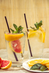 Two glass cups of water with red orange, lemon, mint and ice. Fresh lemonade