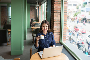 Beautiful cute asian young businesswoman in the cafe, using laptop and drinking coffee smiling