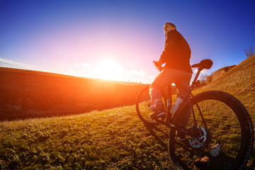 Naklejka na ściany i meble low angle view of cyclist standing with mountain bike on trail at sunset