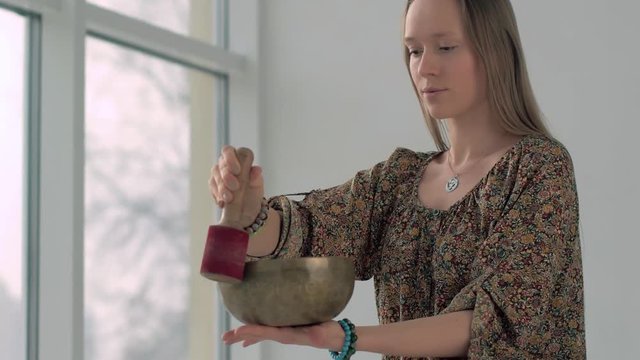 Attractive yoga girl playing the singing bowl while practicing yoga