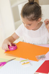 Beautiful little girl cutting paper using decorative drill press on the art lesson class. Children education concept. Kids crafts