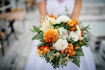 Elegant orange and white wedding bouquet at hands of bride.