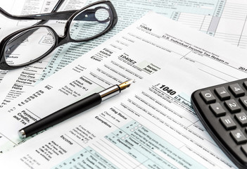 Calculator, glasses and pen on tax form 1040.