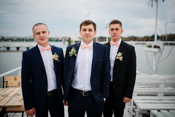 Groom with best mans posed on the pier berth at cloudy wedding day.