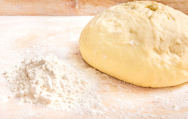 Dough with a pile of flour on a wooden background.