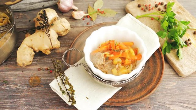 Pouring famous asian noodles soup - lamian  - into white porcelain bowl on wooden kitchen table with soup ingredients - ginger, pepper, noodles, herbs. Top view.