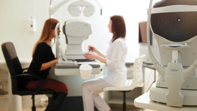 Modern ophthalmologist examining attractive woman's eyes with modern equipment, blured