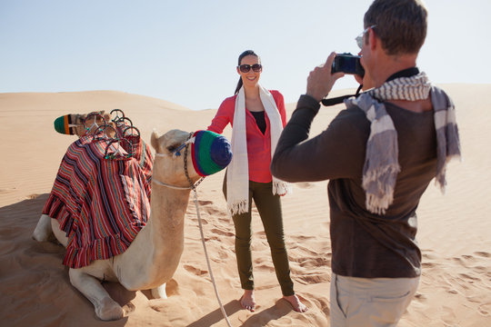 Man photographing woman with camel at desert.