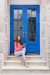 Student girl sitting with a tablet in front of blue doors