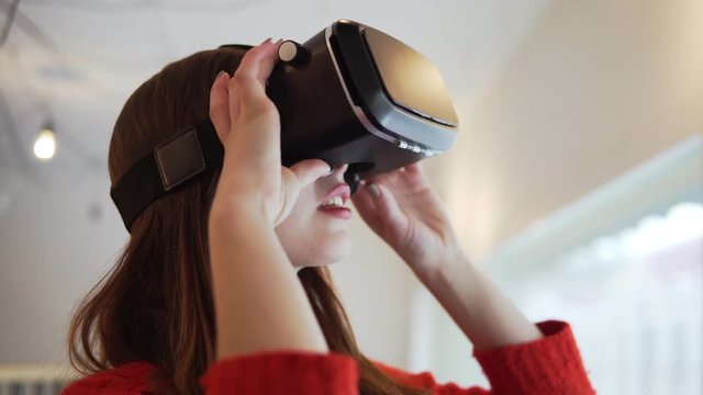 Pretty brunette woman using her mobile phone VR headset at cafe. Affordable virtual reality glasses in action. 4K steadicam video
