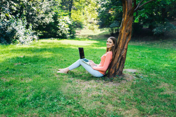 Student girl working with a laptop in a green park