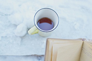 Obraz na płótnie Canvas Yellow tea mug and a brown paper note book in snow 