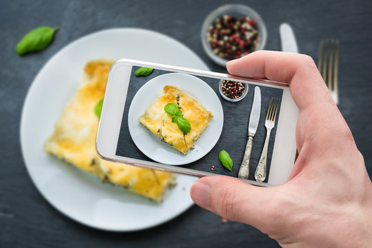 Hand takes shot of fresh lasagna with bechamel sauce with mobile phone