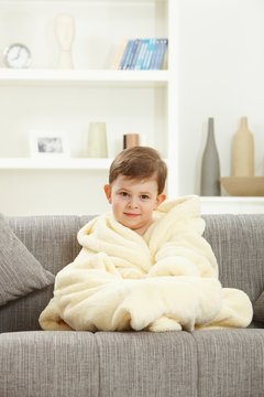 Cute little boy sitting in bathrobe at home sofa