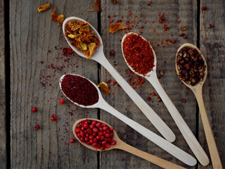 Red spices on a wooden background. Pink pepper, sumac, paprika, marigold, Sichuan pepper.