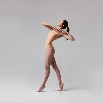 young beautiful ballet dancer in beige swimsuit posing on light grey gradient studio background