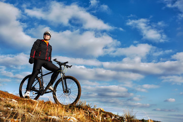 Cyclist riding his bike down on mountain trail. Beautiful sky and clouds on background