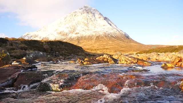 Sunny winter morning at frozen river Coupall at delta to river Etive. Snowy cone of mountain Stob Dearg 1021 metres high. Higland in Scotland an marvelous day. Dry grass and heather bushes on banks. 